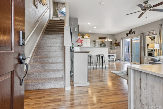 staircase featuring ceiling fan with notable chandelier, wood finished floors, and recessed lighting