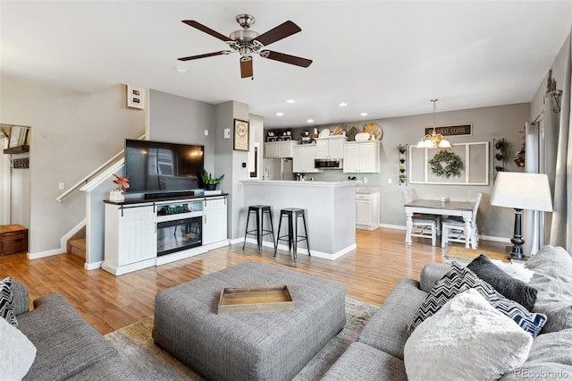 living area with ceiling fan with notable chandelier, light wood-style flooring, recessed lighting, and stairs