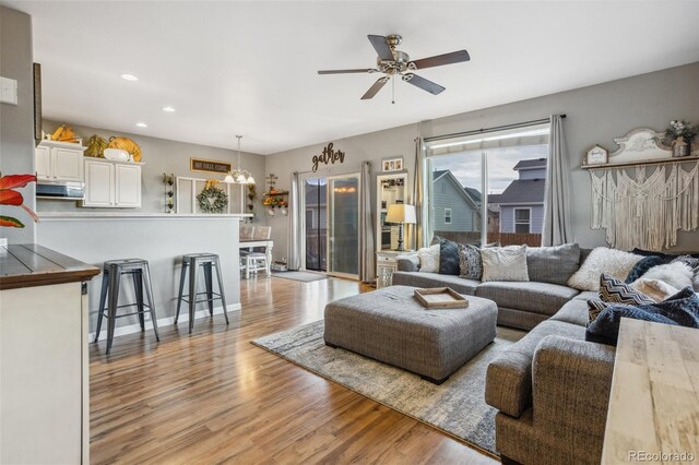 living room featuring light wood-style floors, recessed lighting, baseboards, and ceiling fan with notable chandelier