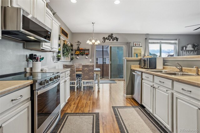 kitchen featuring a chandelier, stainless steel appliances, a sink, white cabinetry, and light wood finished floors