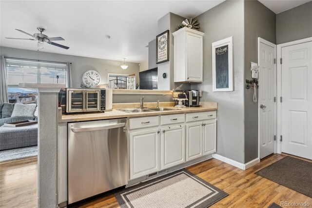 kitchen with white cabinets, stainless steel dishwasher, light countertops, light wood-style floors, and a sink