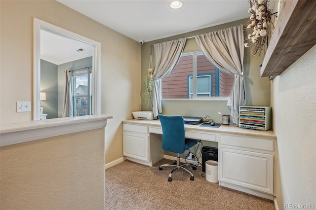 office area featuring light carpet, visible vents, baseboards, and built in study area