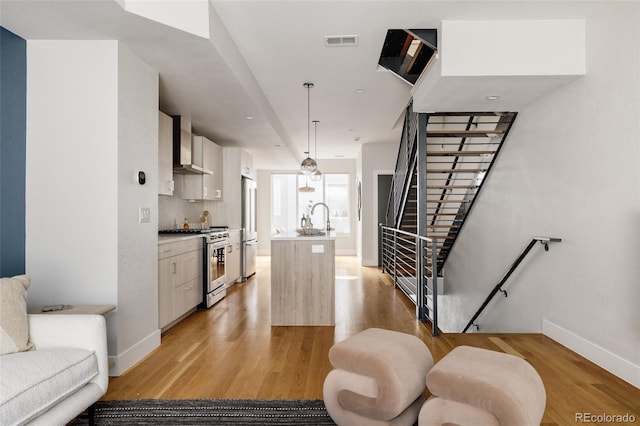 kitchen featuring wall chimney exhaust hood, light hardwood / wood-style flooring, decorative light fixtures, stainless steel appliances, and sink