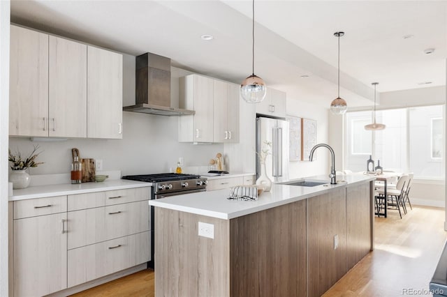 kitchen with sink, wall chimney exhaust hood, light hardwood / wood-style flooring, hanging light fixtures, and high quality appliances