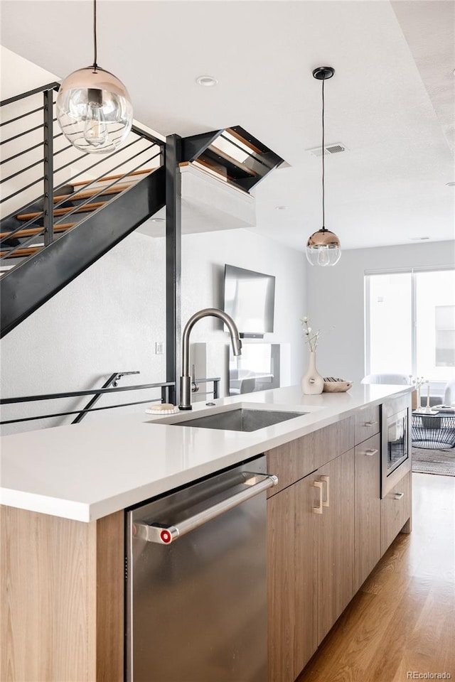 kitchen featuring light wood-type flooring, appliances with stainless steel finishes, pendant lighting, and sink