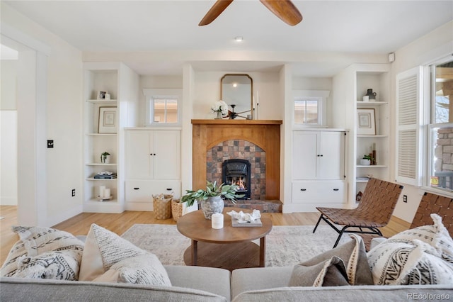 living room featuring ceiling fan, built in shelves, a fireplace, and light hardwood / wood-style flooring