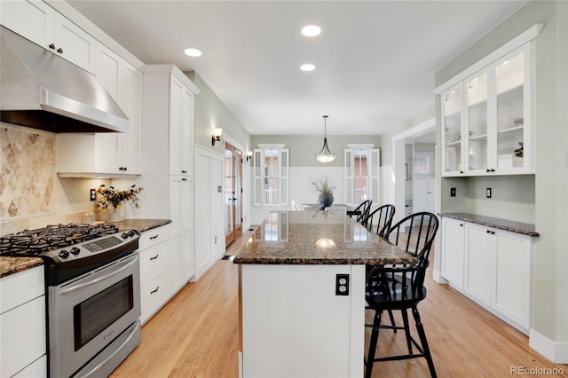 kitchen with a breakfast bar area, range hood, a center island, gas stove, and dark stone counters