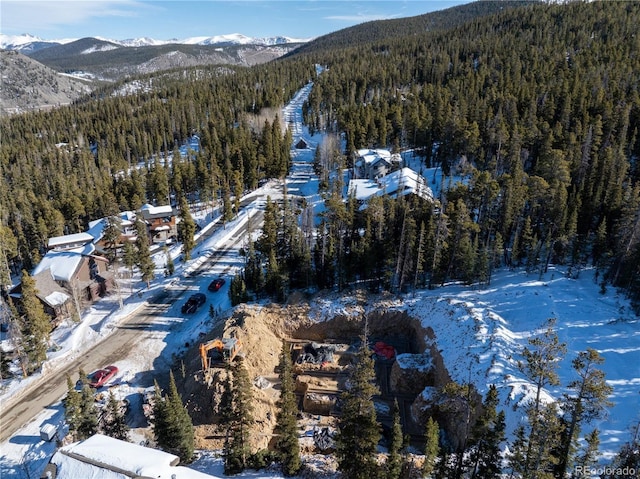 snowy aerial view featuring a forest view and a mountain view