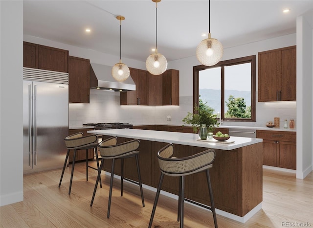 kitchen featuring stainless steel appliances, wall chimney range hood, light wood-type flooring, and light countertops