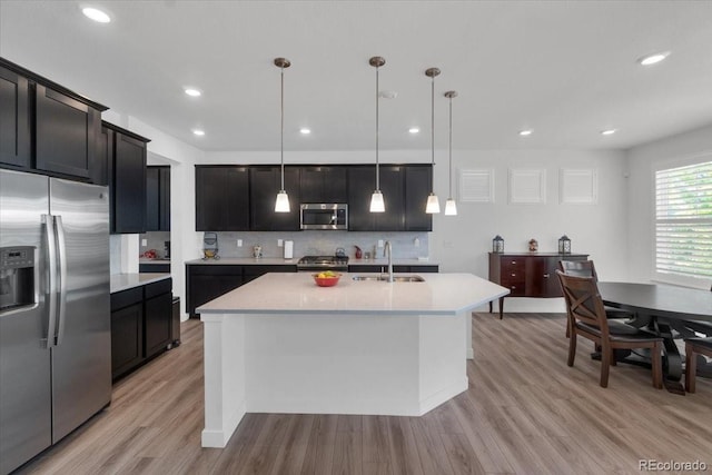 5045 Preserve Pl, Firestone, CO 80504 - kitchen with stainless steel appliances, light countertops, light wood-style flooring, a kitchen island with sink, and backsplash
