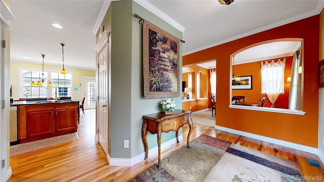 corridor with arched walkways, light wood-type flooring, crown molding, baseboards, and recessed lighting