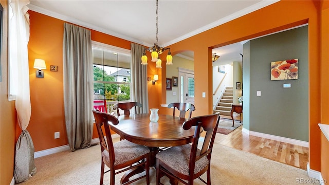 dining room featuring crown molding, baseboards, light colored carpet, arched walkways, and stairway