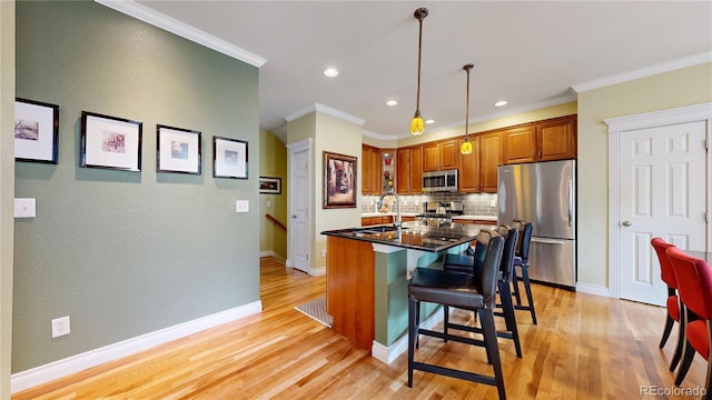 kitchen featuring stainless steel appliances, backsplash, light wood-style floors, brown cabinets, and a center island with sink