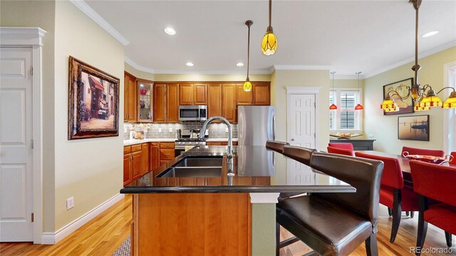 kitchen featuring appliances with stainless steel finishes, a sink, brown cabinets, decorative backsplash, and light wood-type flooring