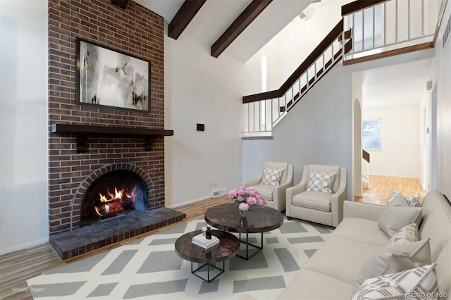 living room featuring a brick fireplace, high vaulted ceiling, light hardwood / wood-style flooring, and beam ceiling