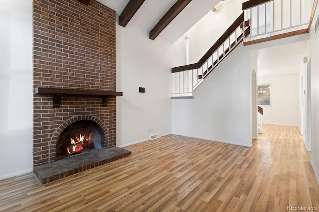 unfurnished living room featuring beam ceiling, a fireplace, high vaulted ceiling, and light wood-type flooring