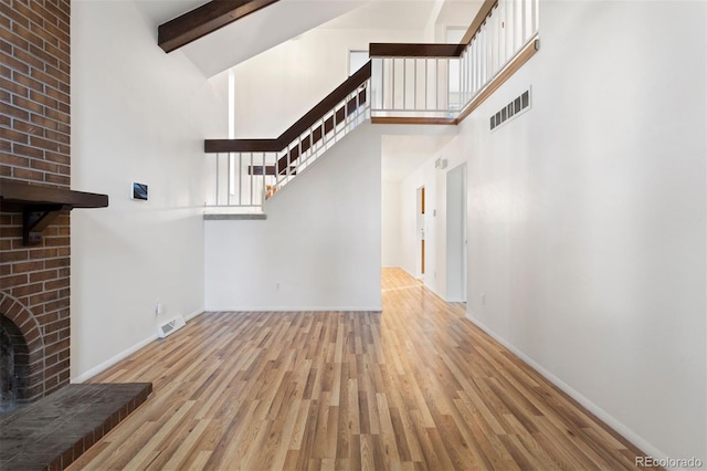 unfurnished living room featuring a high ceiling, beamed ceiling, and light wood-type flooring