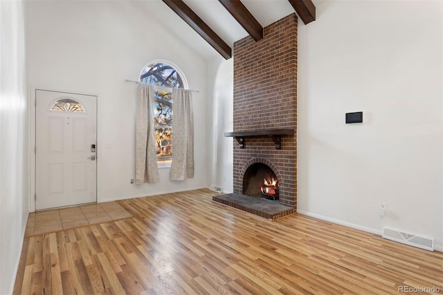 unfurnished living room featuring a fireplace, high vaulted ceiling, light hardwood / wood-style floors, and beamed ceiling