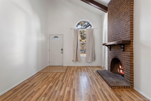 foyer featuring high vaulted ceiling, beam ceiling, light hardwood / wood-style floors, and a brick fireplace