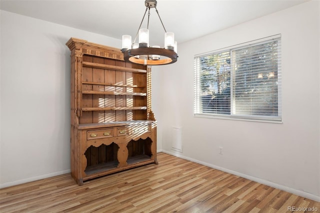 unfurnished dining area with a notable chandelier and light hardwood / wood-style flooring