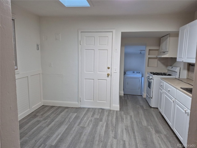 kitchen with a skylight, white cabinetry, gas range gas stove, light hardwood / wood-style flooring, and washer and clothes dryer