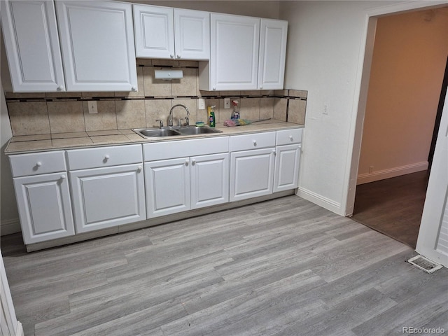 kitchen featuring white cabinets, light wood-type flooring, sink, and tasteful backsplash