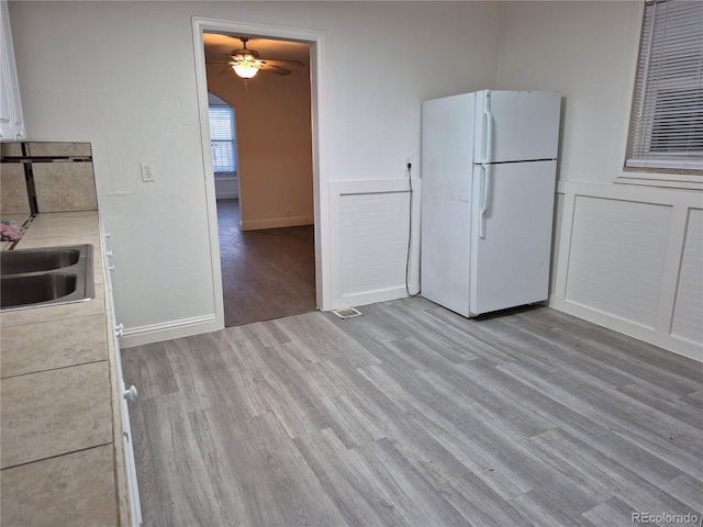 kitchen with ceiling fan, sink, white refrigerator, white cabinets, and light wood-type flooring