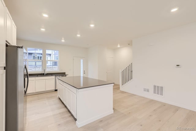 kitchen with light wood-style floors, dark countertops, stainless steel appliances, and visible vents