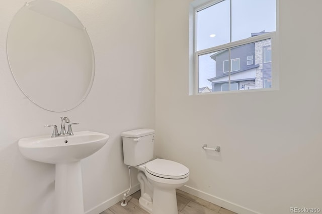 bathroom featuring a sink, baseboards, toilet, and a wealth of natural light