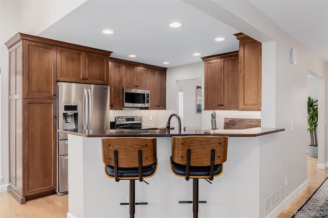 kitchen with appliances with stainless steel finishes, dark countertops, a peninsula, and a breakfast bar area