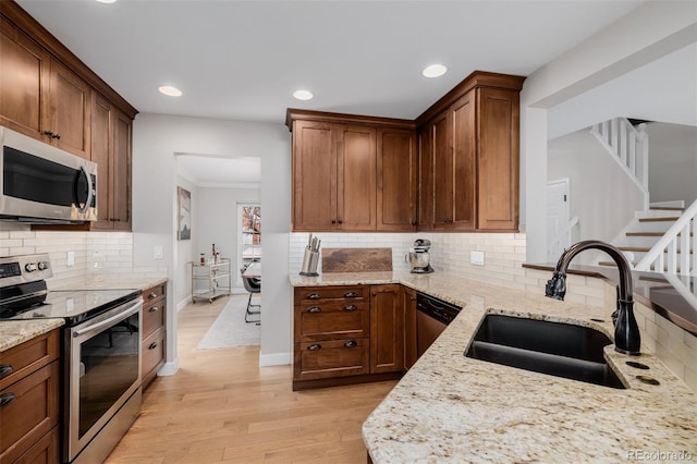 kitchen with light wood-style flooring, appliances with stainless steel finishes, light stone counters, and a sink