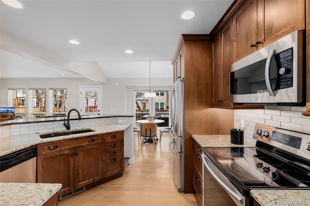 kitchen featuring hanging light fixtures, light stone countertops, appliances with stainless steel finishes, and a sink