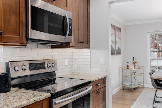 kitchen with appliances with stainless steel finishes, brown cabinets, crown molding, and light stone countertops