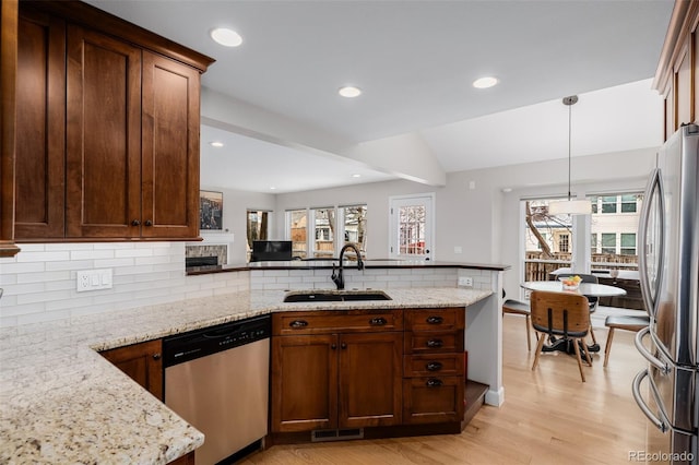 kitchen featuring a peninsula, appliances with stainless steel finishes, light stone counters, and a sink