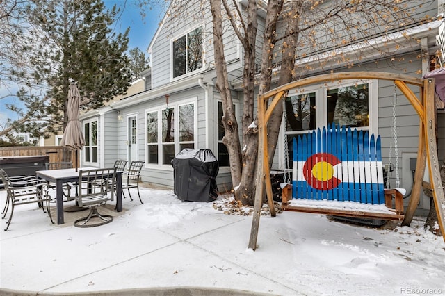 snow covered patio featuring grilling area, fence, and a hot tub