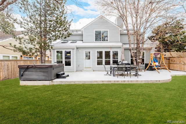 rear view of property featuring a playground, a fenced backyard, a lawn, a patio area, and a hot tub