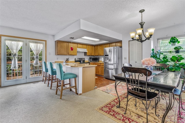 18771 Mexico Dr E, Aurora, CO 80017 - kitchen with appliances with stainless steel finishes, under cabinet range hood, a peninsula, a chandelier, and brown cabinetry