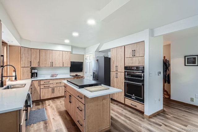 kitchen featuring sink, light wood-type flooring, stainless steel refrigerator with ice dispenser, and black double oven