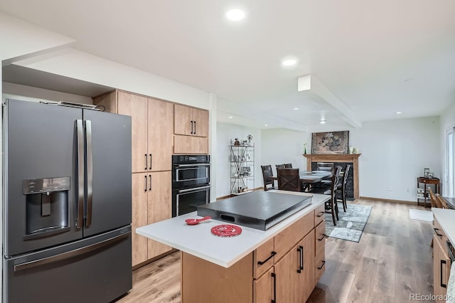 kitchen featuring stainless steel fridge with ice dispenser, a center island, light hardwood / wood-style flooring, and black double oven