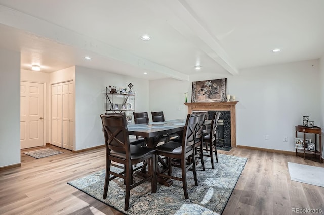 dining room featuring beamed ceiling, light hardwood / wood-style floors, and a premium fireplace