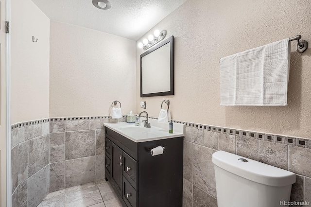 bathroom with vanity, a textured ceiling, toilet, and tile walls