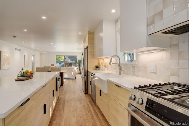 kitchen featuring appliances with stainless steel finishes, tasteful backsplash, sink, light stone countertops, and light wood-type flooring