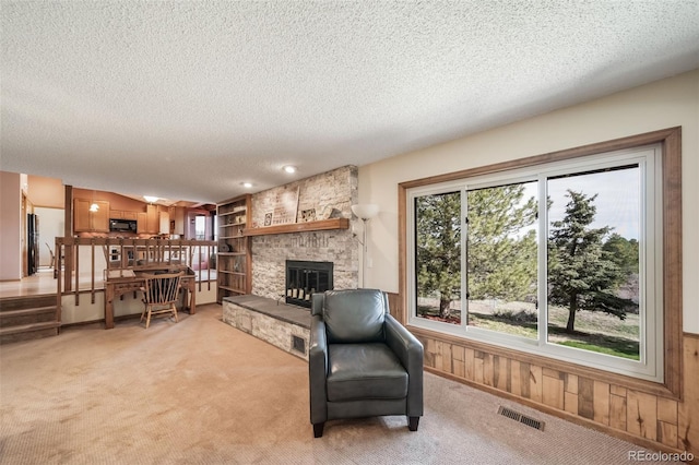 living area featuring a fireplace, light colored carpet, a textured ceiling, and visible vents