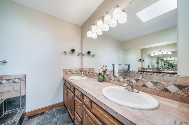 bathroom featuring baseboards, a skylight, visible vents, and a sink
