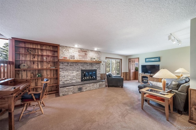 living area featuring a fireplace, a textured ceiling, a wainscoted wall, rail lighting, and carpet