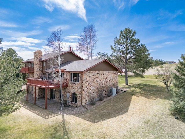 back of house with a deck, roof with shingles, a chimney, brick siding, and a patio area