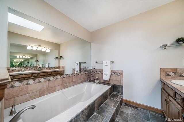 bathroom with a bath, visible vents, a skylight, vanity, and baseboards