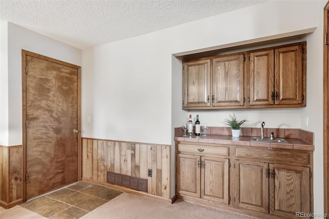 bar with visible vents, indoor wet bar, a textured ceiling, a wainscoted wall, and a sink
