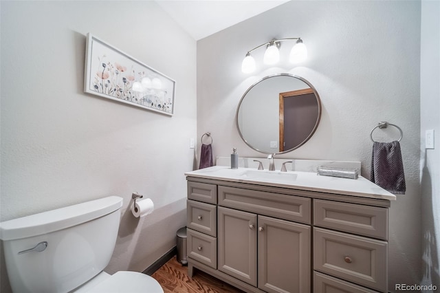 half bathroom featuring vanity, baseboards, toilet, and wood finished floors