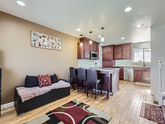 kitchen featuring appliances with stainless steel finishes, decorative light fixtures, tasteful backsplash, a breakfast bar area, and light wood-type flooring